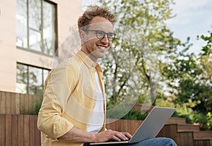 Smiling businessman wearing eyeglasses using laptop computer, planning start up working from home. Successful business and career.