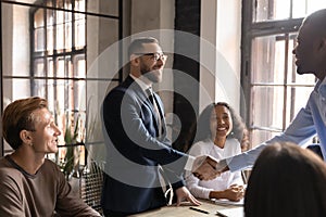 Smiling businessman wearing glasses shaking hands with diverse business partner