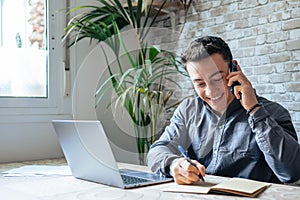 Smiling businessman wearing glasses talking on phone, sitting at desk with laptop, friendly manager consulting customer by phone,