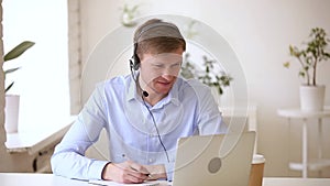 Smiling businessman wearing headset studying online making notes