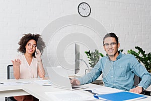 Smiling businessman working on laptop while businesswoman talking