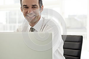 Smiling businessman working on laptop in office - portrait