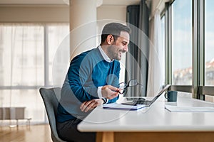 Smiling businessman working on laptop while sitting at office desk