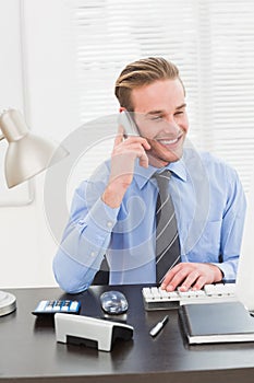 Smiling businessman working and phoning at his desk