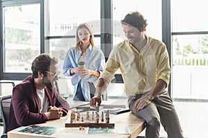 Smiling businessmen playing chess near blurred