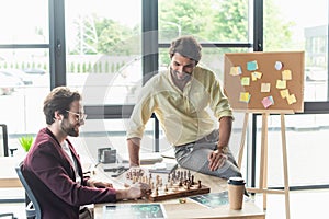 Smiling businessmen playing chess near coffee