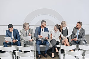smiling businesspeople sitting with documents on stage and talking