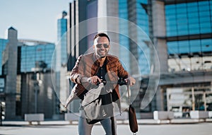 Smiling businessperson on an electric scooter in the city with briefcase and sunglasses