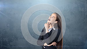 Smiling businesswoman with arms folded looking up at copyspace. Standing over gray background.