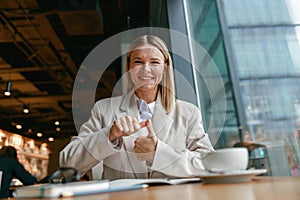 Smiling businesswoman communicating in sign language while looking at camera while sitting in cafe