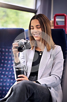 Smiling Businesswoman Commuting To Work On Train Looking At Photos On Retro Digital Camera