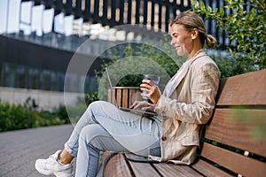 Smiling businesswoman drinking coffee and work on laptop outside of office. Distance work concept