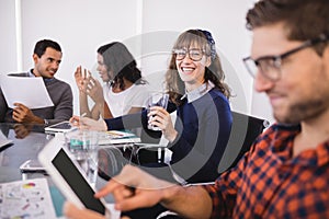 Smiling businesswoman with drinking glass sitting by colleagues