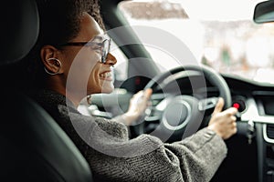 Smiling businesswoman driving car and holding both hands on steering wheel on the way to work