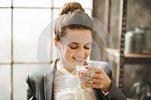 Smiling businesswoman enjoying cup of coffee latte macchiato