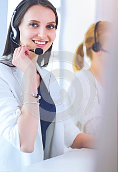 Smiling businesswoman or helpline operator with headset and computer at office