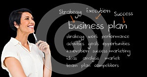 Smiling businesswoman holding pen and standing against blackboard with business terms