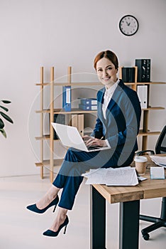 smiling businesswoman with laptop sitting on table
