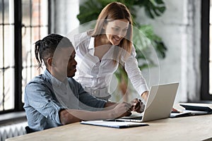 Smiling businesswoman mentor helping new African American employee with software