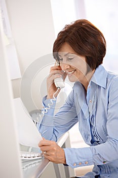 Smiling businesswoman on phone call reading paper.