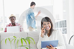 Smiling businesswoman phoning and using tablet on sofa