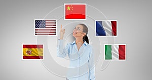 Smiling businesswoman pointing upwards standing by flags against gray background