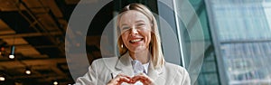 Smiling businesswoman showing heart shape with gesture while working in cafe near window