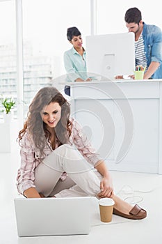 Smiling businesswoman sitting on the floor using laptop