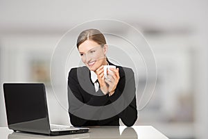 Smiling businesswoman sitting with laptop computer, holding coffee and tea mug