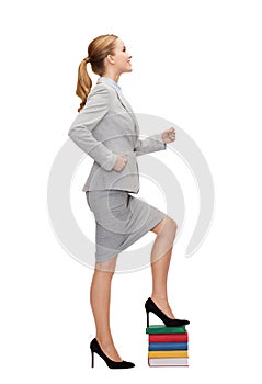 Smiling businesswoman stepping on pile of books