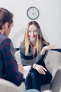 Smiling businesswoman in suit giving interview to journalist and gesturing