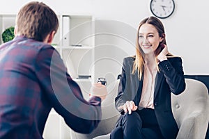 Smiling businesswoman in suit touching hair while giving interview to journalist