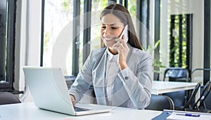 Smiling businesswoman talking on mobile phone and using laptop in office