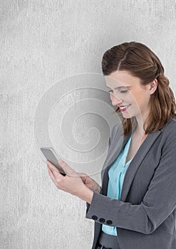 Smiling businesswoman texting on smart phone against wall