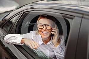 Smiling businesswoman traveling on back seat of car and talking smartphone while looking at window