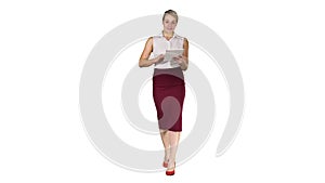 Smiling businesswoman using electronic tab swiping and looking to the camera while walking on white background.