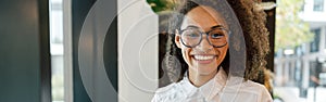 African businesswoman working laptop while standing near window in coworking and looking camera