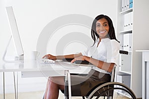 Smiling businesswoman in wheelchair working at her desk