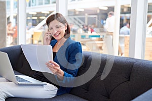 Smiling busineswoman on couch with phone, laptop and paperwork