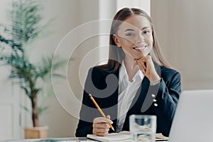 Smiling bussiness woman sitting by desk looking at camera