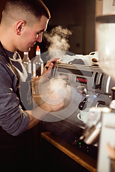 Smiling male barista using professional coffee machine enjoying job in cafe improving skills of making cappuccino