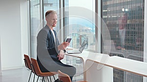 Smiling busy business man sitting in office holding cellphone using phone.