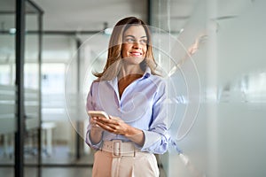 Smiling busy business woman of middle age using mobile phone standing in office.