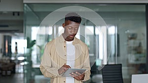Smiling busy young Black business man using tablet standing in office.