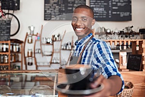 Smiling cafe barista offering up a fresh cup of cappuccino