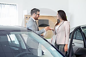 Smiling car salesman handing over your new car keys. Happy girl the buyer.