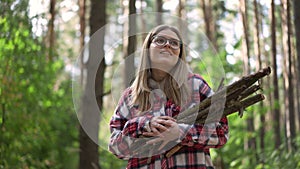 Smiling carefree woman walking in forest with firewood branches looking around. Portrait of relaxed happy traveler