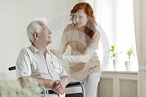 Smiling caregiver helping disabled senior man in a wheelchair