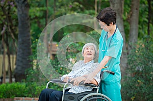 Smiling caregiver Senior nurse take care a Senior patient on wheelchair for relaxing and looking around park photo