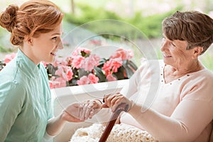 Smiling caregiver supporting happy senior woman with walking sti